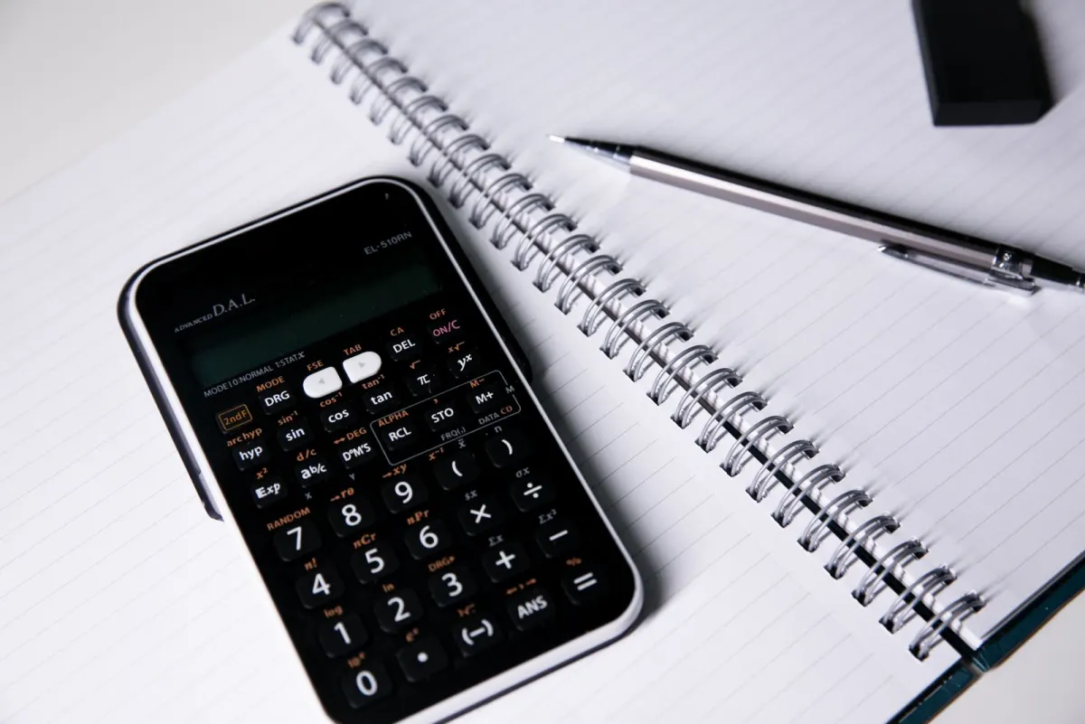 A black scientific calculator and a pencil on an open spiral notebook with blank lined pages