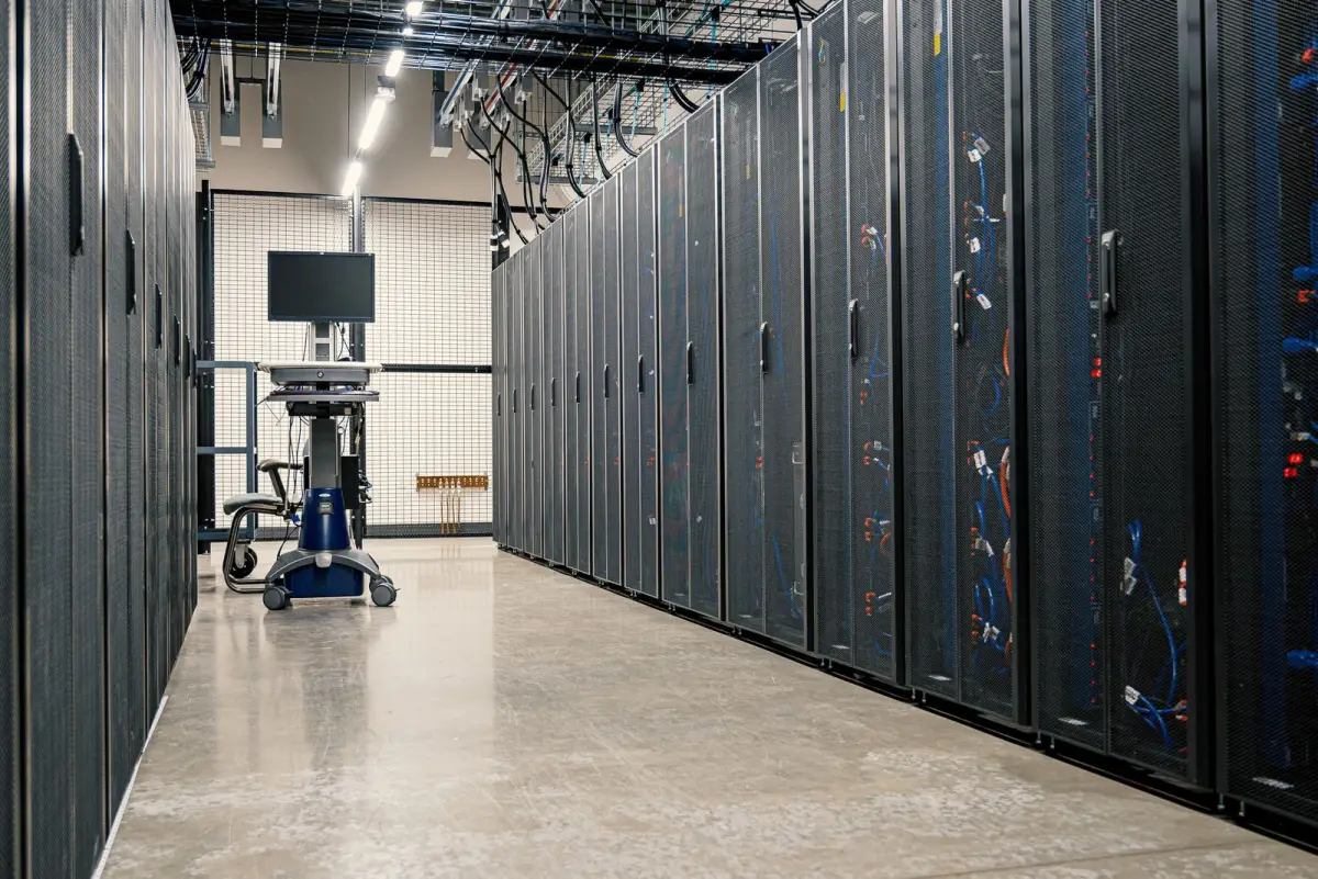 A long aisle of server racks in a data center with a monitor on a cart at the far end