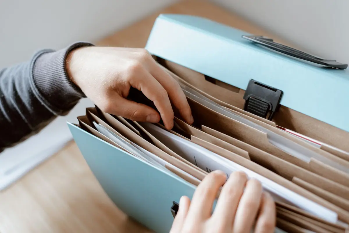 Two hands sorting paper documents in a blue expanding file folder